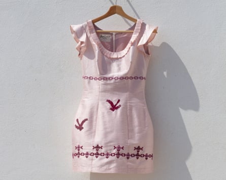 A pink dress with red embroidered birds against a whitewashed wall outdoors. A pink dress with red embroidered birds against a whitewashed wall outdoors.
