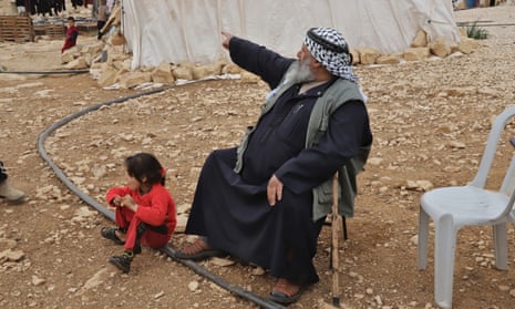 A man sitting with a young girl at his feet points off into the distance