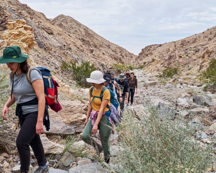 people hike uphill in a line among the hills - the landscape is dry and brown