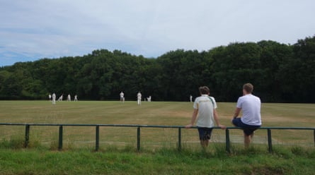 Two teenagers sit on a fence watching a cricket match
