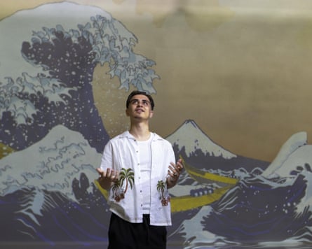 Young man stands inside an immersive version of Great Wave by Hokusai which shows a large wave crashing and Mount Fuji.