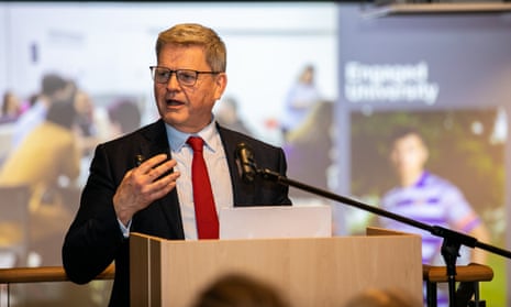 Robert Van de Noort, the vice-chancellor of the University of Reading – he is giving a speech at a wooden lecturn behind a microphone, and wears a dark jacket, white shirt and red tie