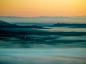 A vast dawn landscape with fog and mountains visible in between, and a church in the distance