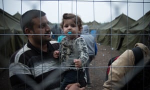 A Syrian refugee carrying his child in a camp near the Hungary-Serbia border where they are being fingerprint registered. 