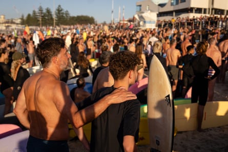 A father and son stand close among thousands on Bondi beach at sunrise