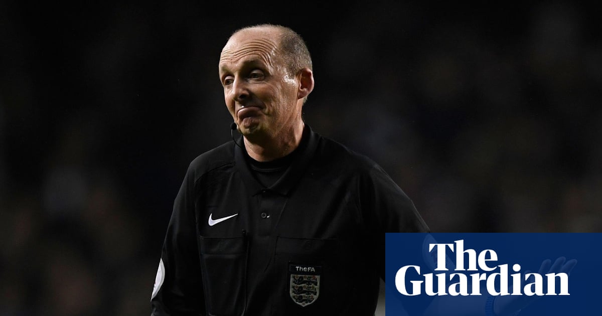 Mike Dean observa una jugada durante un partido de la Premier League con el silbato en la mano.