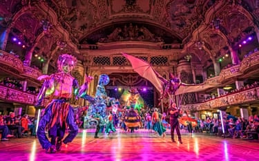 People perform with large puppets in front of an audience in a grand ballroom