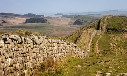 Wide stone wall, about six to eight courses deep and topped with grass, follows the curves of hills to the distance