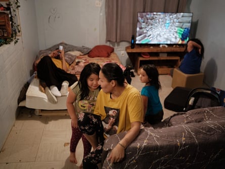 Isabel Boyce sits in a small room with three small girls; one is watching television. A fourth older girl lies on a mattress looking at a phone screen.