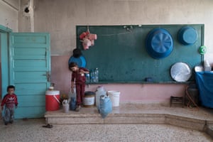 A girl fills jugs and buckets with water in the courtyard of Mousab bin Omayer school in Tell Tamr, a town in north-east Syria