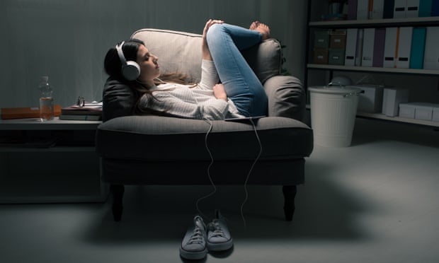 Young woman curled up on a chair listening with headphones.