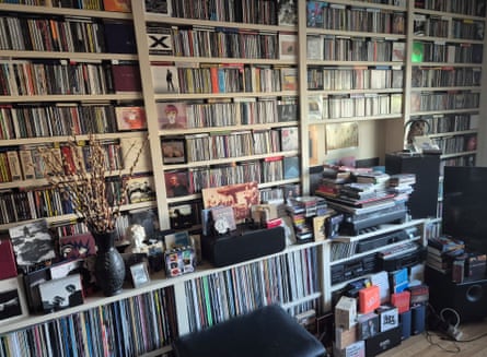 Floor-to-ceiling shelves of Andrew Wales’s CD collection fill a room, with stacks piled on a cabinet