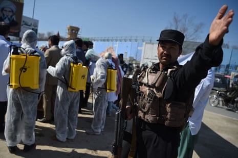 An Afghan policeman gestures as volunteers wearing a hazmat suits and facemasks gather on before the start of a preventive campaign against the spread of the Covid-19 in Kabul