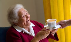 Happy elderly lady receives a cup of tea from carer companion