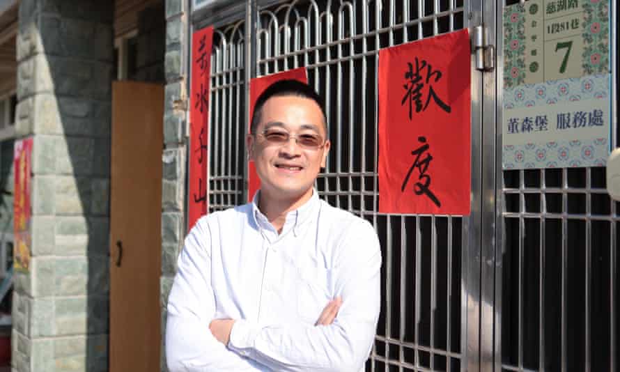 Tung Sen-po standing by a gate with Chinese signs hanging on it in the street