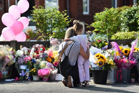 A mother hugs her daughter in front of flowers and balloons.