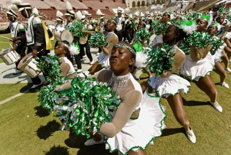 Cheerleaders in white and green costumes with shiny green and silver pompoms.