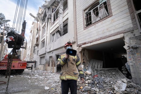 एक अग्निशमन कर्मी एक क्षतिग्रस्त इमारत के सामने लाउड स्पीकर के माध्यम से बात कर रहा है