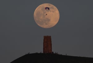 A paraglider flies past the full moon near Glastonbury Tor in Glastonbury, England.