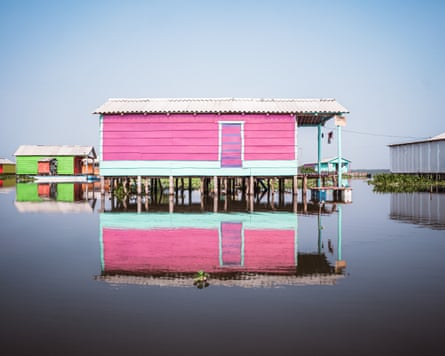 A single-storey wooden building painted bubblegum pink on stilts over placid water