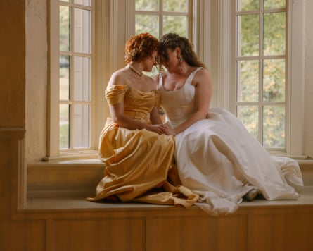 two women seated on ledge near window hold their heads together