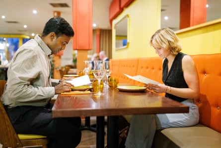 Eshwar and Georgia sit at a restaurant table, perusing their menus