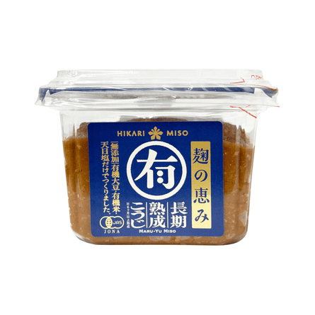 A clear plastic container of brown miso paste with a blue Hikari Miso label