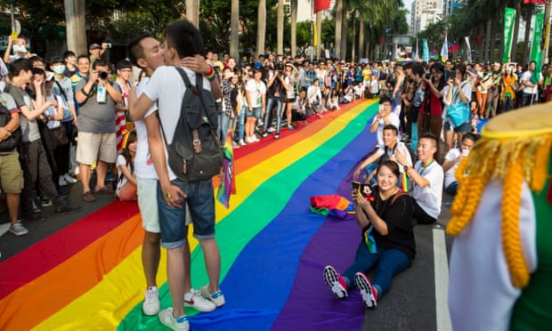 Two gay men kiss standing on the rainbow banner during the annual gay pride march through Taipei’s city streets.