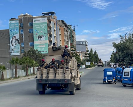 Soldiers sit on the back of a pickup truck driving down a deserted street past local taxis.