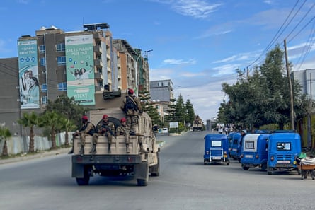 Soldiers sit on the back of a pickup truck driving down a deserted street past local taxis.