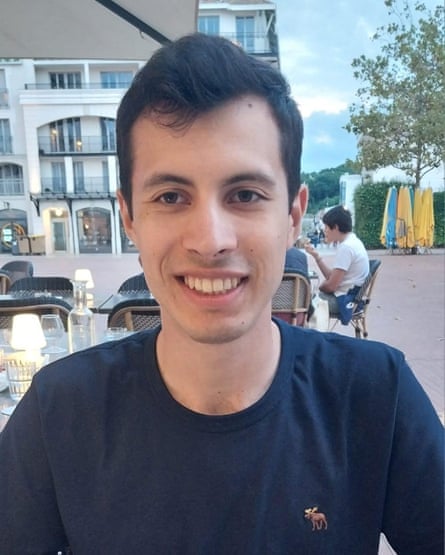 Quentin Deranque smiles as he sits at an outdoor table of a cafe or restaurant