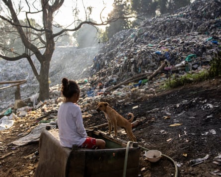 A girl sits next to a dog next to an area covered with rubbish