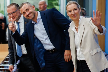 Alice Weidel, Ulrich Siegmund and Tino Chrupalla pose for the media during a press conference in Berlin: she is waving and Siegmund is doing a thumbs up. All three are smiling.