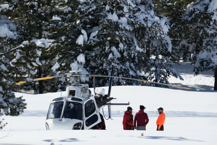 Three people on a snowy hillside with snowy trees and a helicopter