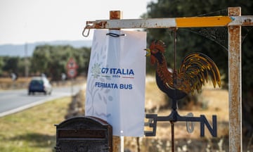 A weather vane and a sign bearing the G7 logo by a road in Italy