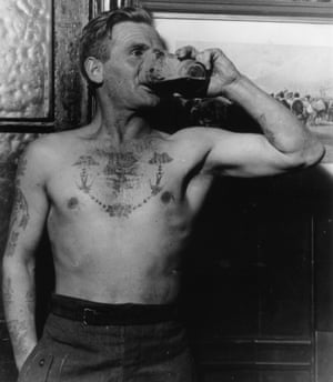A man enjoying a beer in a public house in the East End of London is stripped to the waist showing off tattoos on his chest and arms