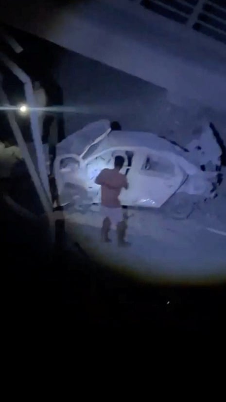 A man looks at a damaged vehicle in the vicinity of the bridge.