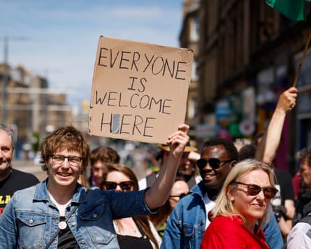 A group of people, one of them holding a cardboard sign reading ‘everyone is welcome here’