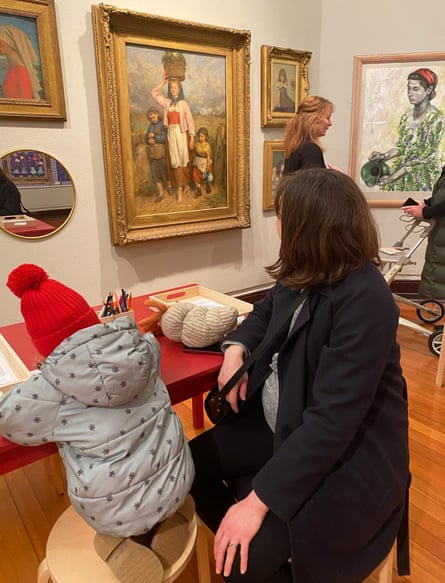 Caroline Walker at Kirkcaldy Galleries. She looks at a painting, while a child sits beside her and draws at a table