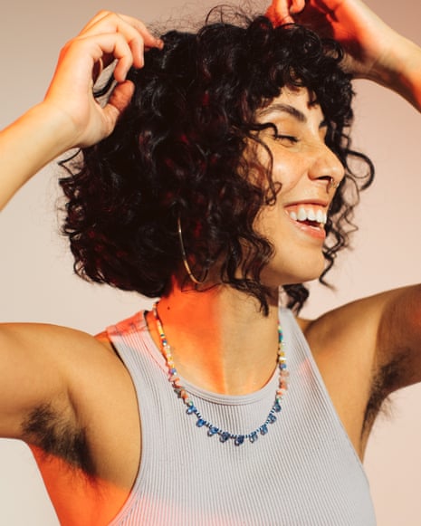 A woman with curly hair laughs joyfully, hands raised, showing unshaven underarms