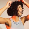 A woman with curly hair laughs joyfully, hands raised, showing unshaven underarms