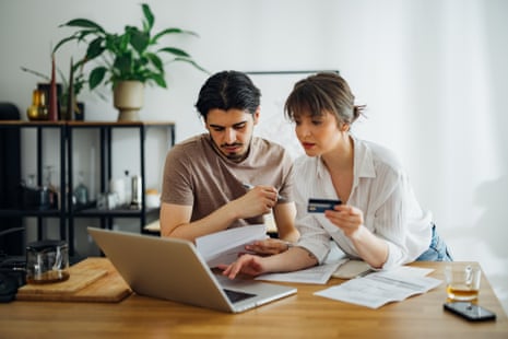 A couple review bills and a credit card together while using a laptop