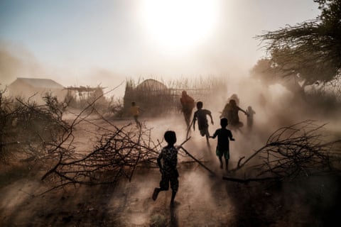 Women and children silhouetted against the sun with dust rising around them