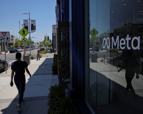 A person walking on a street past an office with the Meta logo displayed on a mirrored frontage