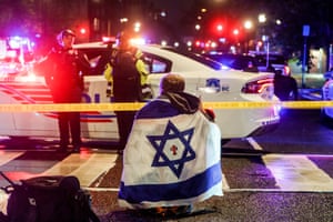 Man sits near police car with Israeli flag draped over his shoulders