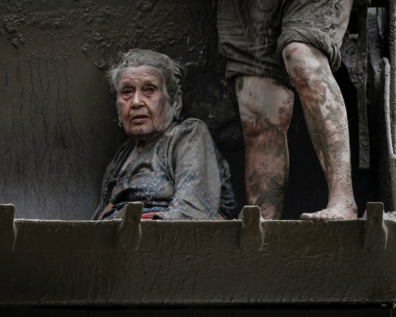 An elderly man covered in mud sitting in the bucket of a digger