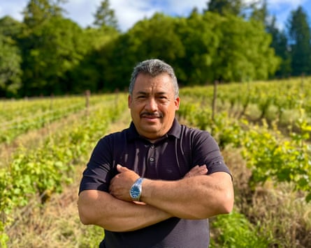 A middle-aged man stands in a vineyard with his arms crossed