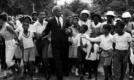 An older black man in a suit surrounded by an enthusiastic crowd