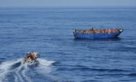 A patrol boat heads towards a boat overcrowded with migrants.