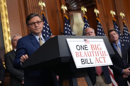 a man looking at a camera at a dais that says ‘One Big Beautiful Bill Act’